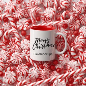 May include: A white mug with a red interior, featuring the text "Merry Christmas" in black script, sits amidst a festive arrangement of red and white peppermint candies and candy canes. The mug also has the text "Eskomockups".
