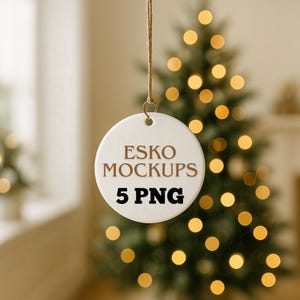 May include: A white ceramic ornament with the text "ESKO MOCKUPS 5 PNG" in brown lettering hangs from a twine string. The background features a blurred Christmas tree with glowing lights.