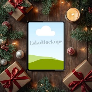 May include: A tablet with a screen showing a sky and landscape scene, surrounded by Christmas decorations. The scene includes wrapped gifts with red ribbons, baubles, pine branches, and a lit candle on a wooden surface. The tablet screen displays the text "EskoMockups".