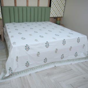 Könnte beinhalten: Weißes Bettlaken mit einem Blumenmuster in Grün- und Beigetönen. Das Bettlaken liegt auf einem Bett mit einem grünen Kopfteil. Das Blumenmuster wiederholt sich über die gesamte Oberfläche, mit einem gestreiften und floralen Rand.