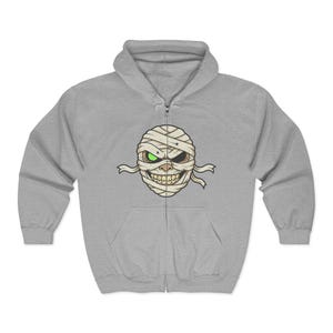 May include: A light grey zip-up hoodie with a mummy face graphic. The mummy face has a bandage design with one green eye and one brown eye, and a wide, toothy grin. The hoodie has a hood and a front pocket.