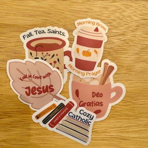 May include: A collection of die-cut stickers featuring autumn-themed mugs, a leaf with the text Fall in love with Jesus, and a stack of books. The mugs display text including Fall. Tea. Saints., Morning Brew, Morning Prayer, and Deo Gratias.