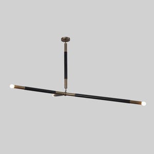 May include: Modern linear chandelier with a black and brass finish. The light fixture has a central vertical support and two horizontal arms, each with a light at the end. The design is minimalist and elegant, suitable for various interior styles.