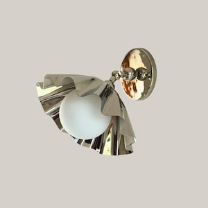 May include: A wall-mounted light fitting featuring a polished silver-tone metal base and a matching ruffled, scalloped metal shade. A spherical, opaque white glass globe bulb is positioned in the centre of the shade, extending from a jointed arm.