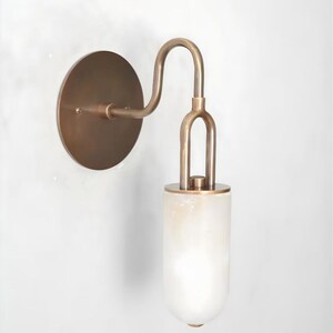 Könnte beinhalten: Wandleuchte mit kreisförmiger Bronze-Rückplatte und gebogenem Arm. Der Arm trägt einen Schirm aus Milchglas. Die Leuchte hat eine warme Ästhetik, die sich für die Innenbeleuchtung eignet.