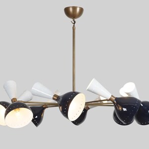 May include: A mid-century modern chandelier with a brass finish. It features black and white cone-shaped shades with small perforations, and a central brass rod for hanging. The light fixtures are evenly spaced.