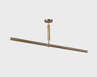 May include: A modern, brass-toned ceiling light fixture. The fixture features a horizontal bar with a light bulb on one end and a central connection point. The light is suspended from the ceiling by a vertical rod.