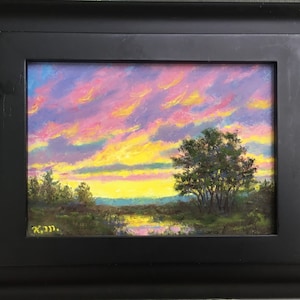 Puede incluir: Pintura de paisaje original enmarcada en negro. La obra representa una vibrante puesta de sol con tonos amarillos, rosas y morados. Un árbol y una zona de hierba están en primer plano, con agua que refleja el cielo.