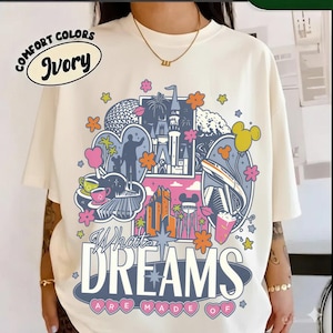 Puede incluir: Camiseta marfil Comfort Colors con un dise&ntilde;o gr&aacute;fico colorido. El dise&ntilde;o presenta un castillo, edificios y el texto "What Dreams Are Made Of". La camiseta tiene cuello redondo y mangas cortas.