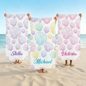 May include: White beach towels with a seashell pattern in various colors. The towels are held up on a sandy beach. The names "Stella", "Michael", and "Victoria" are printed on the towels in different colors.