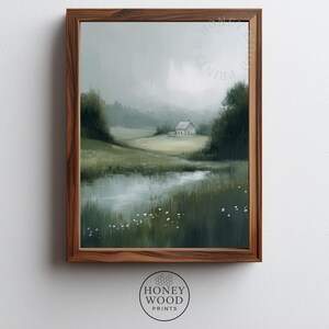 May include: A framed landscape print featuring a serene countryside scene. The artwork depicts a small white house nestled in a green field, with a reflective pond in the foreground. The print is encased in a dark brown wooden frame.