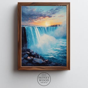 Könnte beinhalten: Ein gerahmter Druck eines Wasserfalls bei Sonnenuntergang. Das Kunstwerk zeigt einen kaskadierenden Wasserfall mit blauem Wasser und weißem Schaum vor dem Hintergrund eines farbenfrohen Himmels mit orangefarbenen und gelben Farbtönen. Der Rahmen ist aus Holz, der Druck von Honey Wood Prints.
