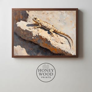 May include: A framed print featuring a detailed painting of a lizard resting on a rock. The lizard has a tan and brown pattern, and the rock is a light beige color. The artwork is in a dark brown wooden frame.