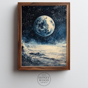 May include: A framed print featuring a celestial landscape. The artwork depicts a large, detailed moon against a dark blue starry sky. The foreground shows a textured, off-white terrain. The frame is made of dark wood. The text "HONEY WOOD PRINTS" is visible.