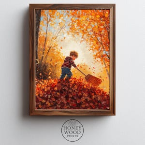 May include: A framed print showing a child raking autumn leaves. The artwork uses warm colours of orange, red, and brown, with a boy in a striped top and blue jeans. The print is from Honey Wood Prints.