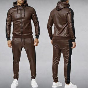 May include: A brown faux leather tracksuit featuring a hooded zip-up jacket and matching pants. The jacket and pants have black stripes down the sides. The tracksuit is a two-piece set.