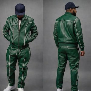 Puede incluir: Un ch&aacute;ndal de cuero verde de dos piezas con ribetes blancos. La chaqueta es de estilo bomber con cierre de cremallera. Los pantalones tienen cintura con cord&oacute;n. La persona lleva una gorra de b&eacute;isbol azul marino y zapatillas blancas.