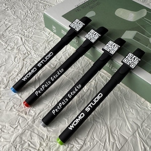May include: Four black pens with QR codes and coloured tips. The pens have the text "WOMO STUDIO" and "PetPals Studio" printed on them. The pen tips are blue, red, grey, and green.