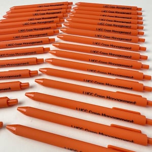 Könnte beinhalten: Eine Ansammlung orangefarbener Kugelschreiber. Jeder Stift trägt den schwarzen Text "LHCC Case Management". Die Stifte liegen auf einer weißen Oberfläche.