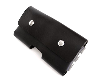 May include: A black leather phone case with a flap closure, secured by three silver rivets. The case has a curved design and is shown against a white background. The case is designed to hold a phone.
