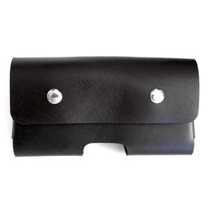 May include: A black leather case with two silver snaps. The case has a cutout for a phone or other device.