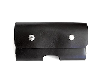 May include: A black leather case with two silver snaps. The case has a cutout for a phone or other device.