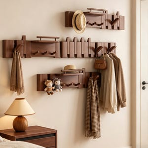 Può includere: Appendiabiti a parete in legno marrone scuro con mensole e ganci. Gli appendiabiti contengono cappelli, sciarpe, borse e vestiti. Una lampada e un comodino sono in primo piano.