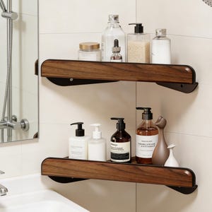 以下が含まれることがあります： 白いタイルの壁に取り付けられた、黒い金属ブラケット付きの2つの木製コーナーシェルフ。シェルフには、ポンプディスペンサー付きのボトル、瓶、装飾品など、さまざまなバスルーム製品が置かれています。シェルフは濃い木目仕上げです。