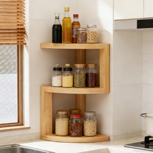 Può includere: Una mensola angolare da cucina a tre livelli in legno chiaro. I ripiani contengono vari barattoli e bottiglie di vetro contenenti spezie, oli e altri alimenti. La mensola è posizionata contro una parete piastrellata bianca.