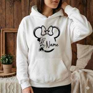 Pu&ograve; includere: Felpa con cappuccio bianca con un design di Minnie Mouse nero, che include fiocco, orecchie e la parola "Name". La felpa ha una tasca a marsupio e un cappuccio con coulisse. Il design &egrave; centrato sul davanti.