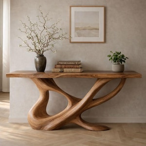 May include: A wooden console table with a unique, organic design. The table features a live edge top and a sculptural base. A bronze vase with white flowers, books, and a small potted plant are on the table.