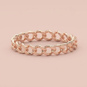Op de afbeelding: Een roségouden ring met een doorlopend schakelontwerp. De band is opgebouwd uit een reeks onderling verbonden, ovaalvormige metalen schakels die een uniforme, flexibel ogende cirkelvormige structuur vormen met een gepolijste, glanzende afwerking.