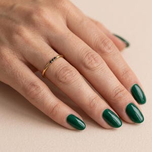 Op de afbeelding: Een dunne gouden ring met drie kleine, ronde, zwarte stenen in een horizontale rij. De ring heeft een gepolijste metalen afwerking en een eenvoudig, slank ontwerp dat comfortabel om de vinger zit en een strakke uitstraling heeft.