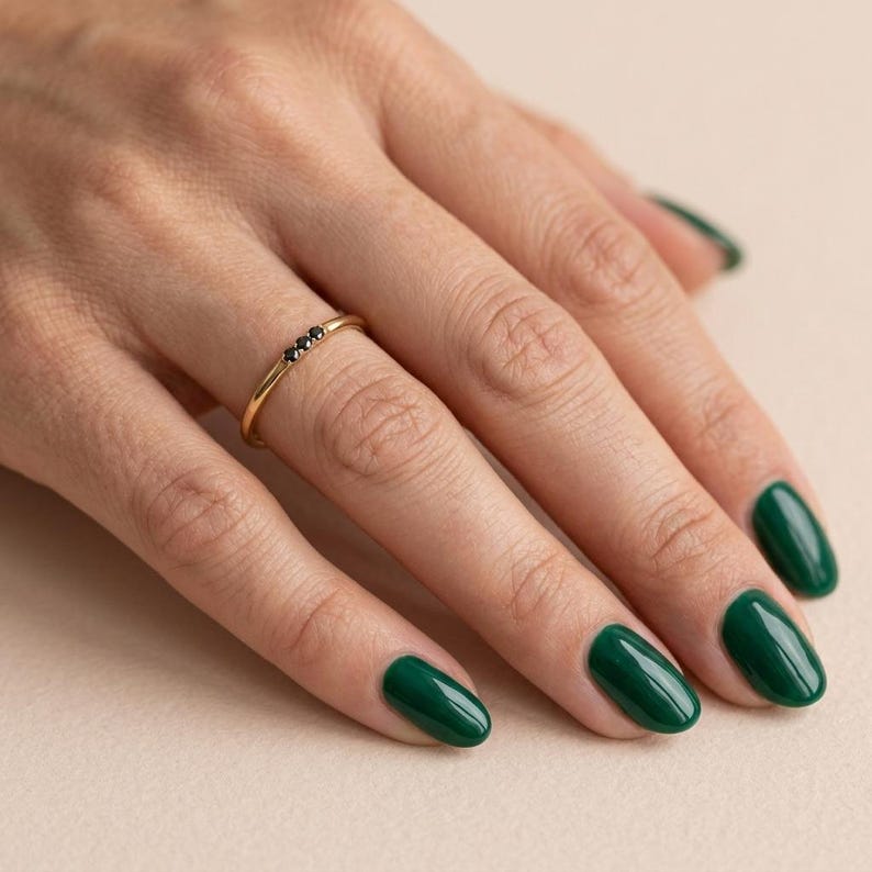 Op de afbeelding: Een dunne gouden ring met drie kleine, ronde, zwarte stenen in een horizontale rij. De ring heeft een gepolijste metalen afwerking en een eenvoudig, slank ontwerp dat comfortabel om de vinger zit en een strakke uitstraling heeft.