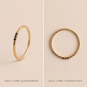 Op de afbeelding: Een dunne gouden ring met drie kleine, ronde, zwarte stenen op een rij. De afbeelding toont de ring vanuit twee perspectieven: een driekwart profielweergave en een direct bovenaanzicht, wat de delicate metalen constructie benadrukt.
