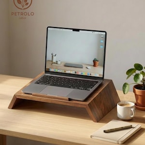 Può includere: Un supporto per laptop in legno scuro con una superficie inclinata che sostiene un laptop argentato. Il supporto presenta una finitura liscia con venature naturali e una base ampia. Lo schermo del laptop mostra uno sfondo desktop e il logo PETROLO labor è visibile nell'angolo in alto a sinistra.