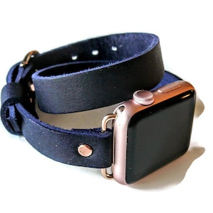 May include: A black leather double wrap watch band with rose gold hardware. The band is designed to fit an Apple Watch.