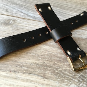 May include: Black leather watch strap with a brass buckle. The strap has a classic design with visible stitching and multiple adjustment holes. The leather appears to be high-quality and durable, suitable for various watch styles.