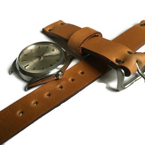 May include: A brown leather watch strap with stitching and a silver buckle. The strap is shown with a silver watch face.