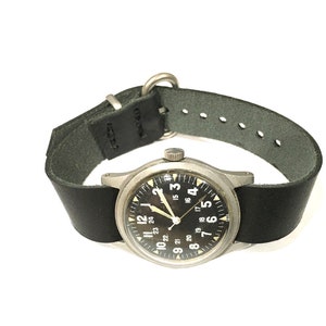 Puede incluir: Un reloj de pulsera plateado con una esfera negra y números blancos. El reloj tiene una correa de cuero negra con costuras blancas.