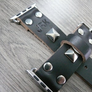 May include: Black leather Apple Watch band with silver studs and a silver buckle. The band has the word "JRK" embossed on it.