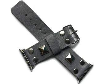 May include: A grey leather watch strap with silver pyramid-shaped studs. The strap has a silver buckle and is designed for a smartwatch.