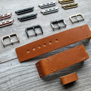 Könnte beinhalten: Eine Auswahl an Armbändern und Hardware für Uhren in Gold-, Silber-, Schwarz- und Roségold-Ausführungen. Die Armbänder sind aus braunem Leder gefertigt. Die Hardware umfasst Schnallen und Verbindungsstücke.