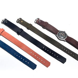 May include: Five leather watch straps in blue, orange, black, olive green, and dark brown. Each strap features a silver-toned metal buckle and a series of adjustment holes. One dark brown strap is attached to a round silver-cased wristwatch.