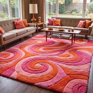 May include: A large rectangular area rug featuring a thick, plush texture with a repeating pattern of swirling, interconnected waves in vibrant shades of hot pink, light pink, and bright orange, covering the floor in a living room setting.