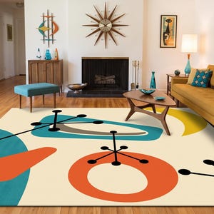 May include: A rectangular area rug featuring a cream-coloured background with a pattern of teal, orange, and yellow abstract shapes. The design includes black linear elements with circular ends, creating a geometric composition across the surface.