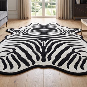 Può includere: Un tappeto a forma di pelle animale caratterizzato da un motivo a strisce zebrate bianco e nero ad alto contrasto. Il tappeto presenta un contorno irregolare e organico che imita la silhouette naturale di una pelle di zebra, con spesse strisce nere.