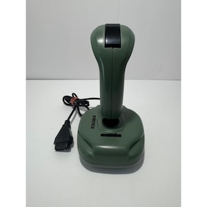 May include: An olive green gaming joystick featuring a tall, ergonomic handle with a black top button. The base includes two black adjustment wheels and a black wired cable with a multi-pin connector attached to the side of the controller unit.