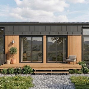 Peut inclure: Petite maison moderne avec un toit et un bardage en métal gris foncé, et des accents en bois naturel. Elle dispose de grandes portes et fenêtres vitrées, d'une terrasse en bois et d'un petit patio avec une chaise. La maison est entourée de verdure et d'un chemin de gravier.