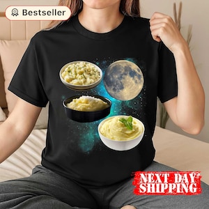 May include: Black t-shirt featuring a graphic design of three bowls of mashed potatoes and a moon. The design includes a blue and green galaxy background. The shirt has a "Bestseller" label and "NEXT DAY SHIPPING" text.